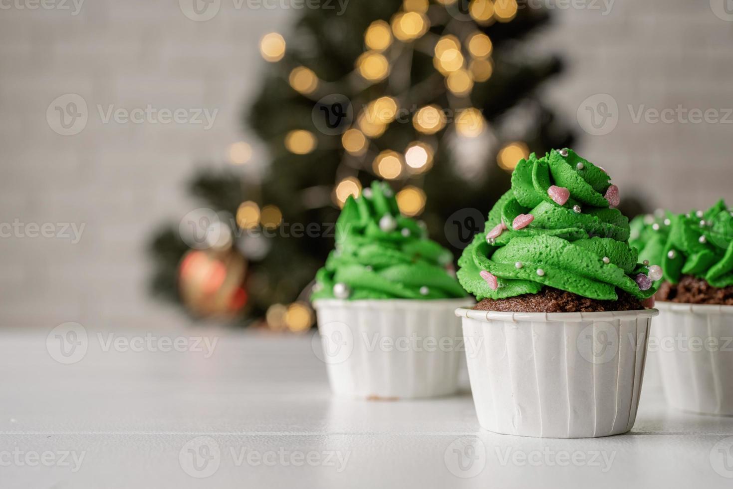 cupcakes em forma de árvore de natal, rodeados de decorações festivas e luzes no fundo foto