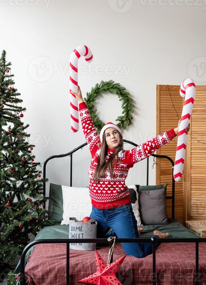 jovem de suéter vermelho e chapéu de Papai Noel dançando na cama celebrando o natal foto