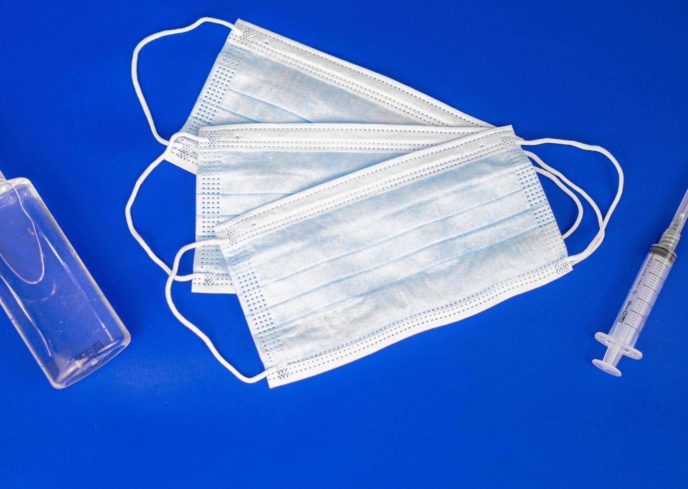 fundo azul com uma seringa, um frasco de desinfetante para as mãos e duas máscaras médicas. o equipamento essencial de cuidados médicos. foto
