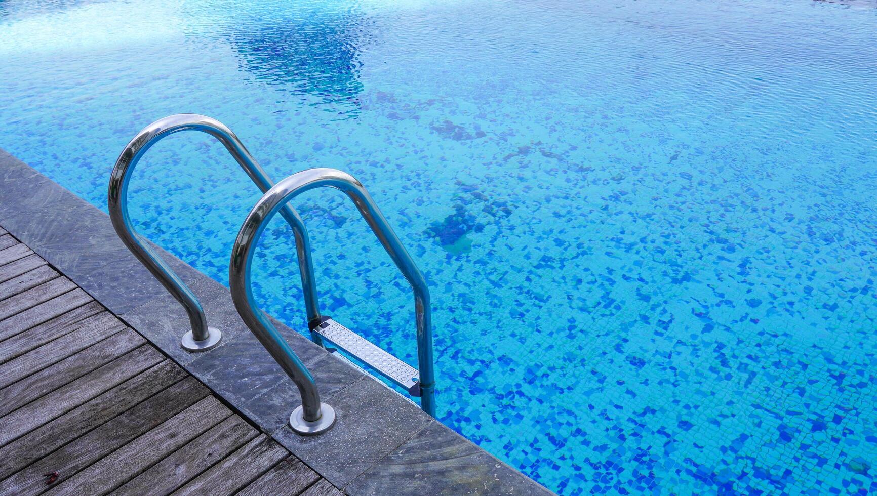 uma piscina de água límpida possuindo um corrimão no rebordo. férias com natação e aproveitando o conceito de verão. uma piscina pública. foto