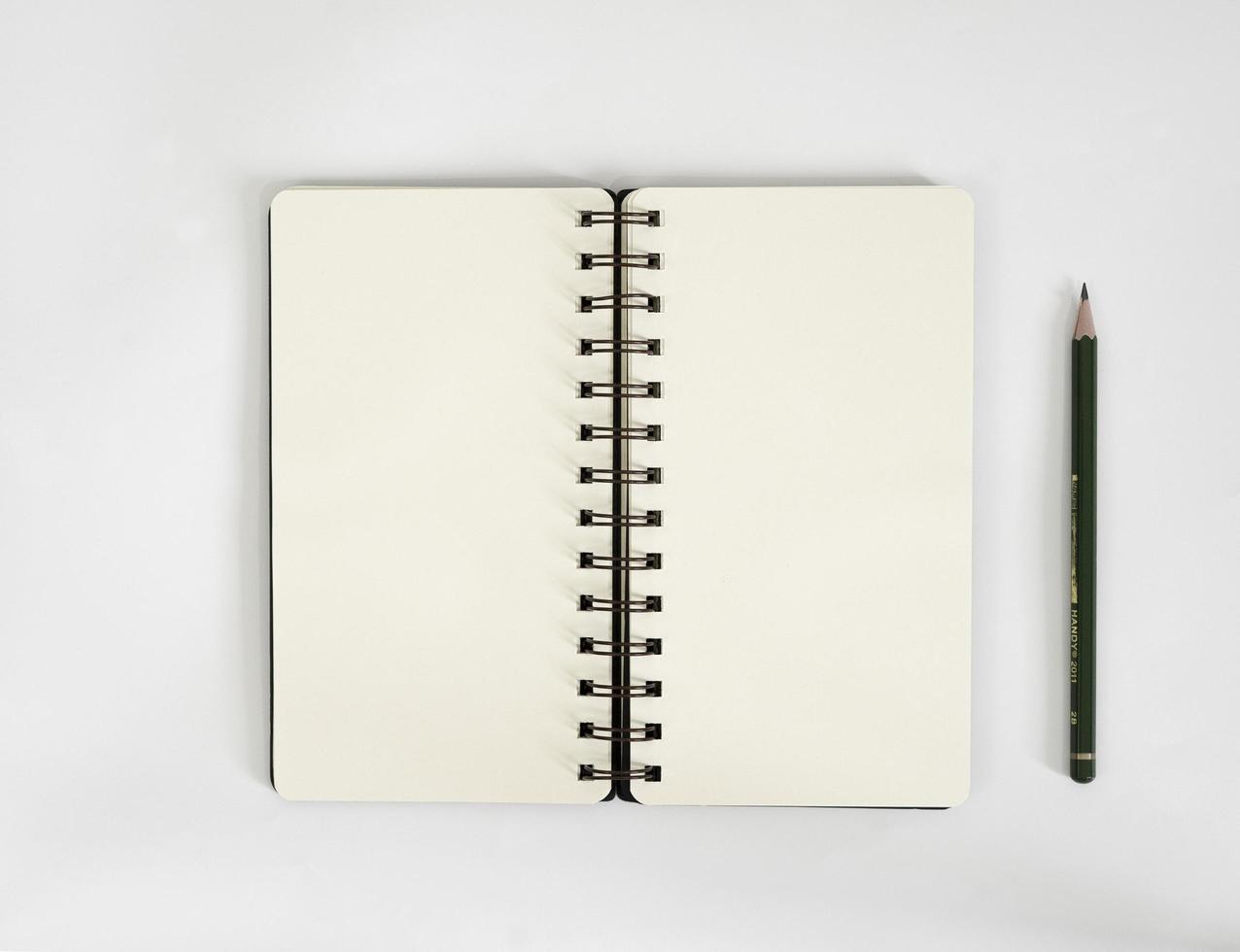mesa branca com caderno e lápis em cima dela. uma maquete de notebook na mesa como um layout de área de trabalho. objeto de escritório isolado no fundo branco. foto