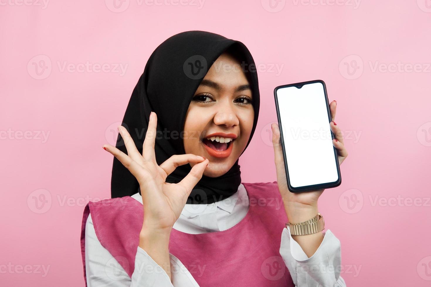 close-up de bela e alegre jovem muçulmana segurando smartphone com tela branca ou em branco, promovendo app, promovendo algo, isolado, conceito de publicidade foto