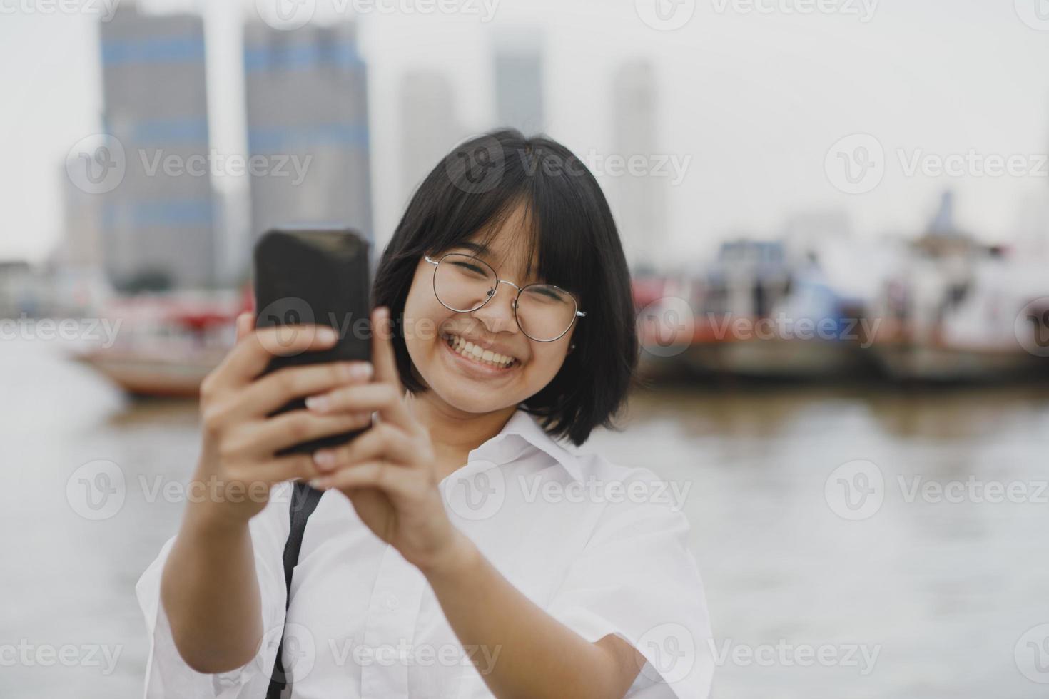 adolescente asiático com dentes sorrindo enquanto tira uma foto com o celular