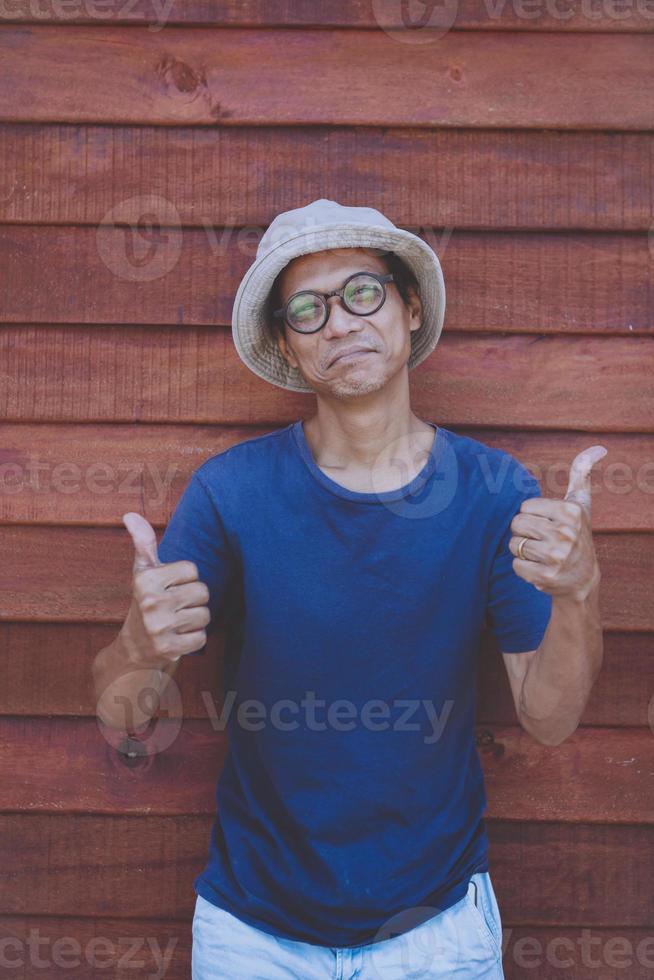 homem asiático assinar bom polegar com uma cara engraçada contra um fundo de madeira velho foto