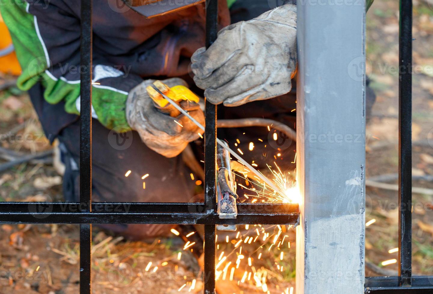 um trabalhador soldador trabalha com metal, solda uma cerca de metal em um parque de outono. foto