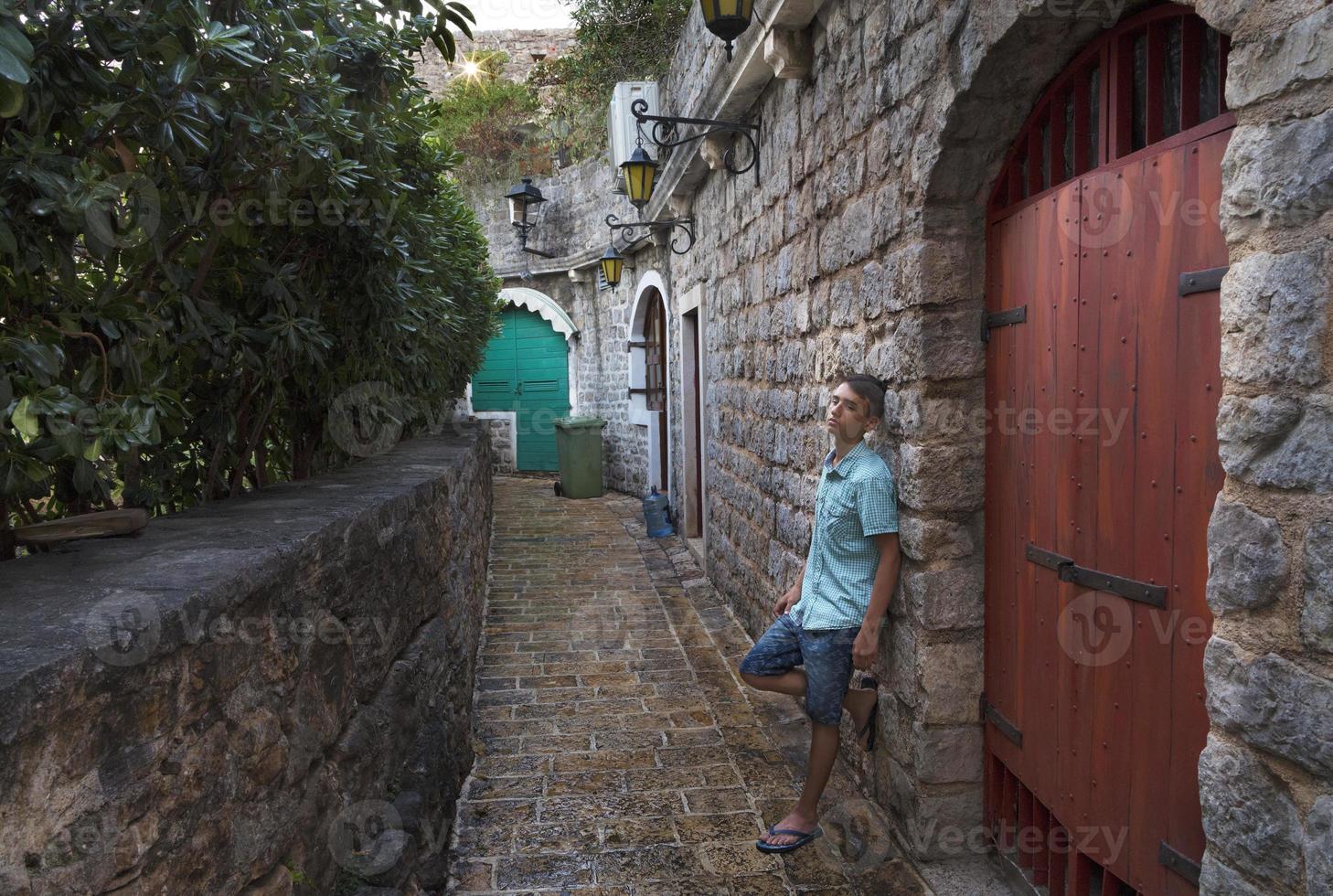 o jovem fica perto do portão de madeira na rua estreita da cidade velha de budva, montenegro. foto