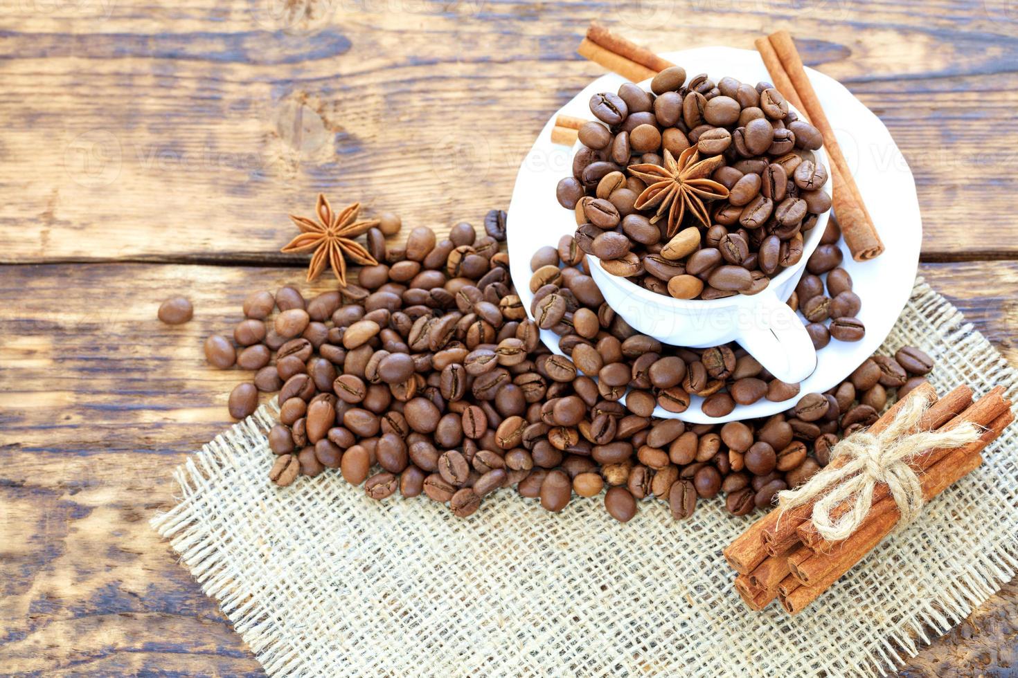 grãos de café em uma xícara sobre um fundo de madeira. canela em um guardanapo e amarrada com barbante. estrelas de anis complementam o aroma do café. foto