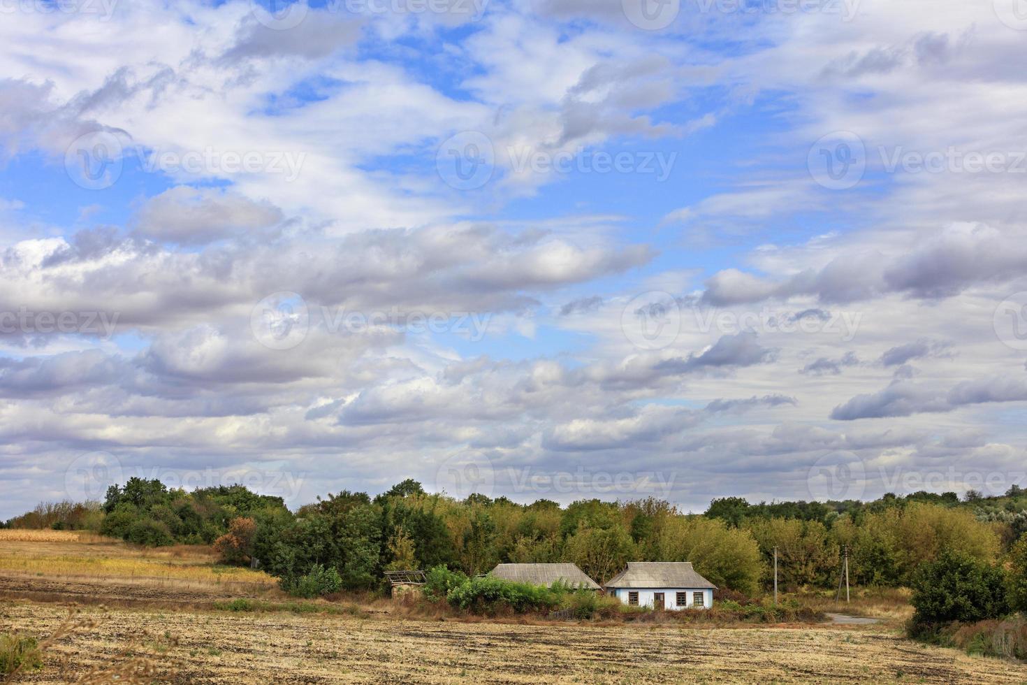 uma casa rural abandonada fica ao lado de uma estrada rural à beira de um campo sob um céu nublado. foto