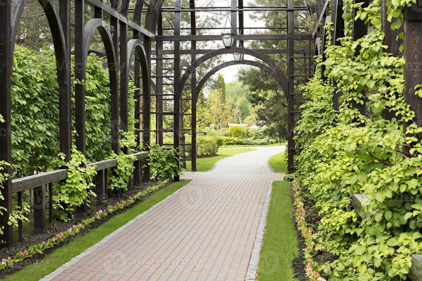 um gazebo de madeira de alta qualidade cercado por um belo arbusto, um gramado bem cuidado e flores foto