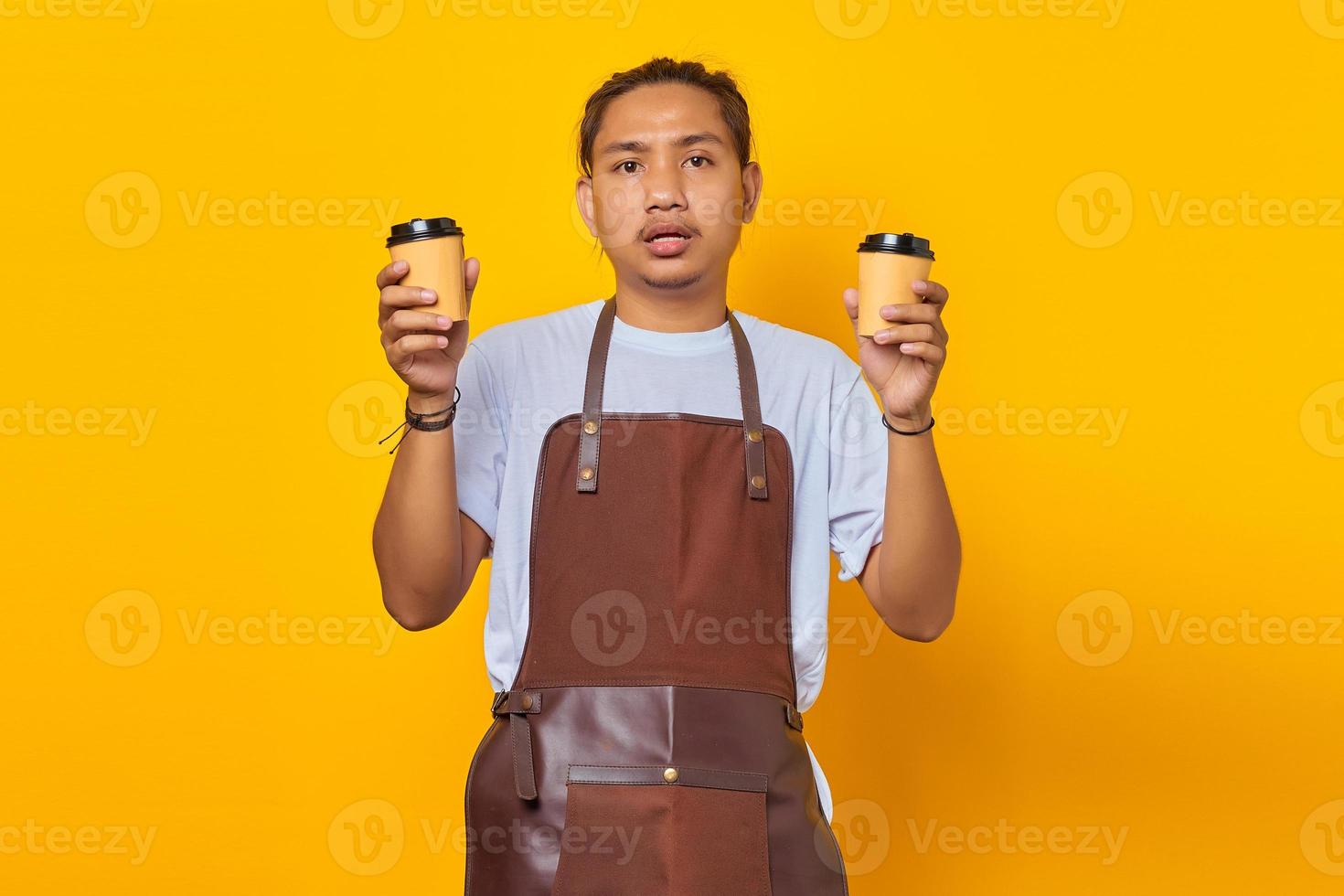 retrato de homem bonito confuso segurando duas xícaras de café e olhando para o futuro, isolado em um fundo amarelo foto