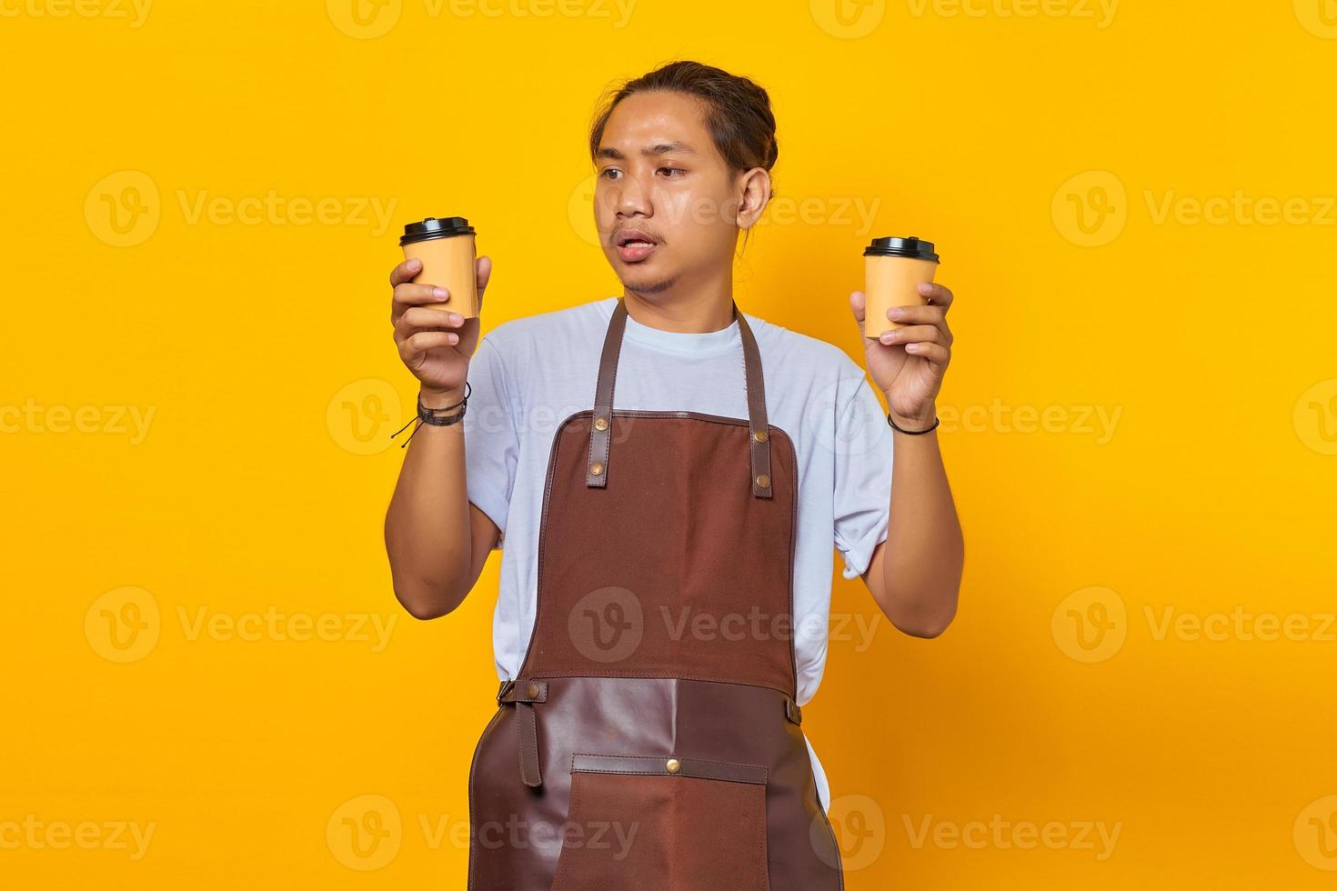 retrato de homem bonito confuso segurando duas xícaras de café e olhando para o futuro, isolado em um fundo amarelo foto