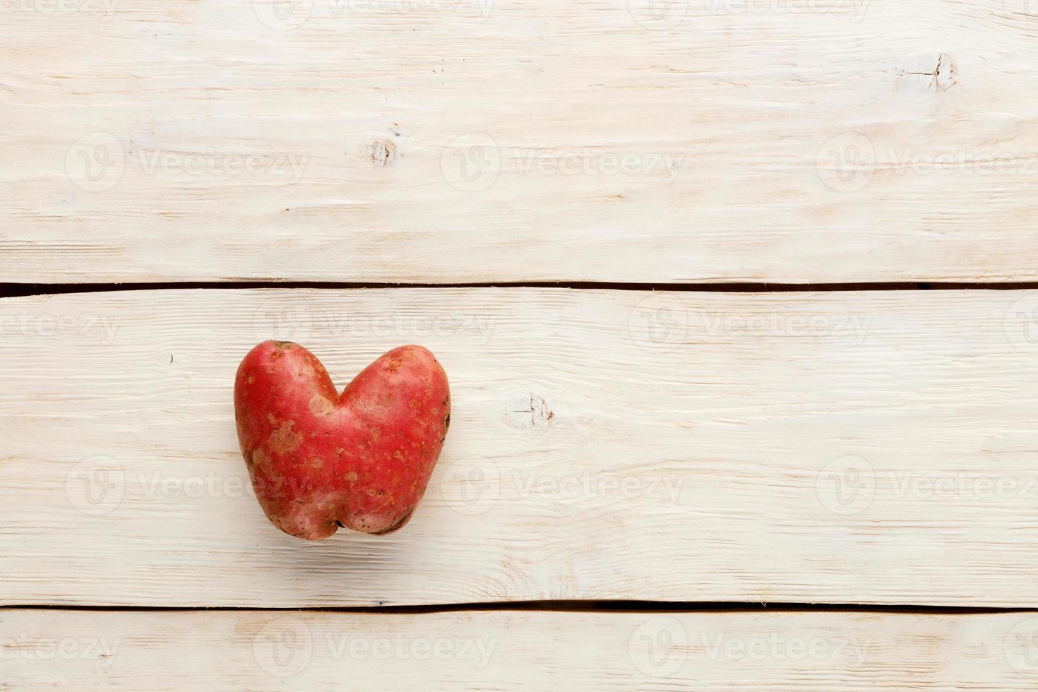 batata feia em forma de coração em um fundo branco de madeira. conceito de resíduo vegetal ou alimentar. vista de cima, close-up. foto
