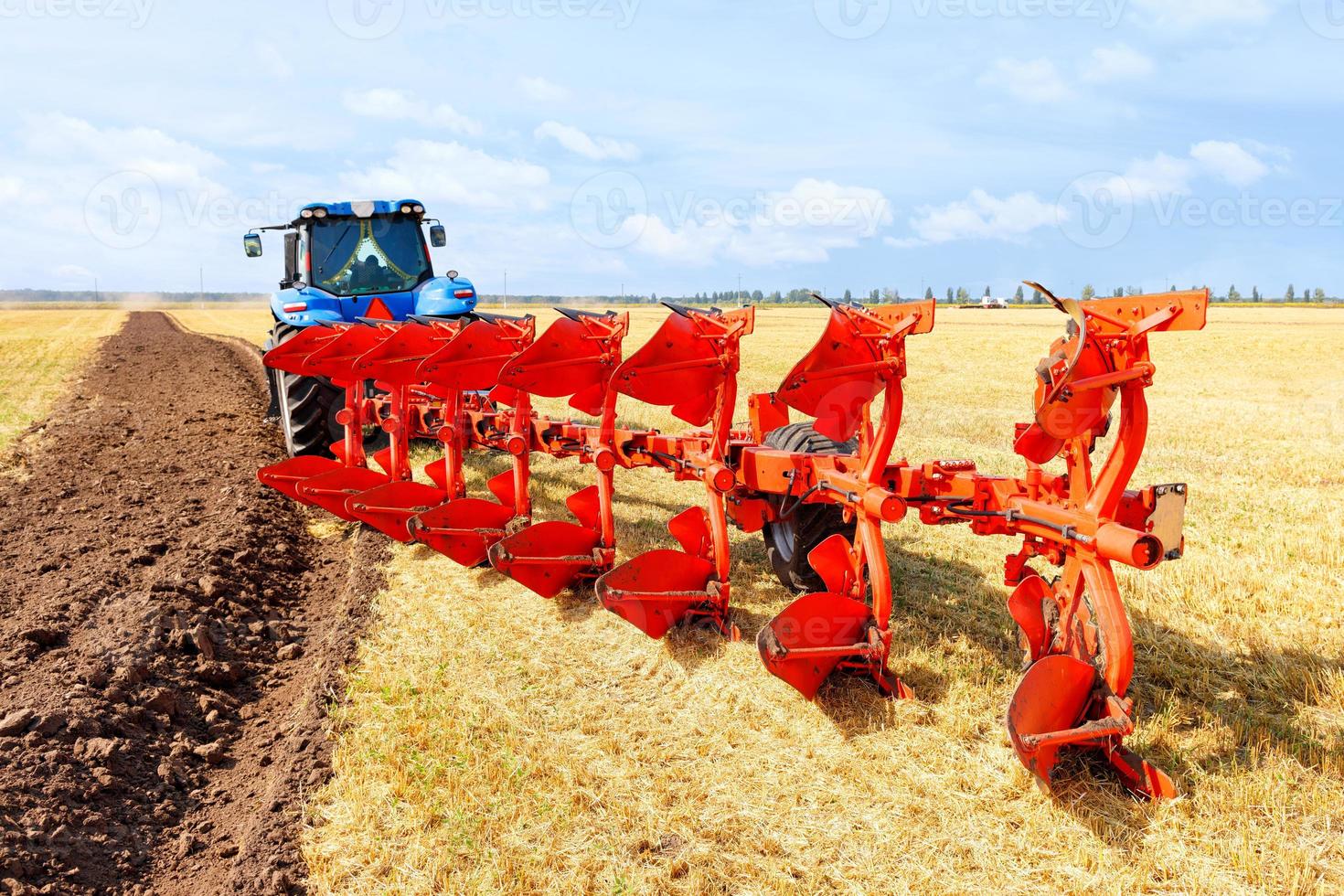 trator agrícola acoplado a um arado de metal em um campo de trigo colhido. foto