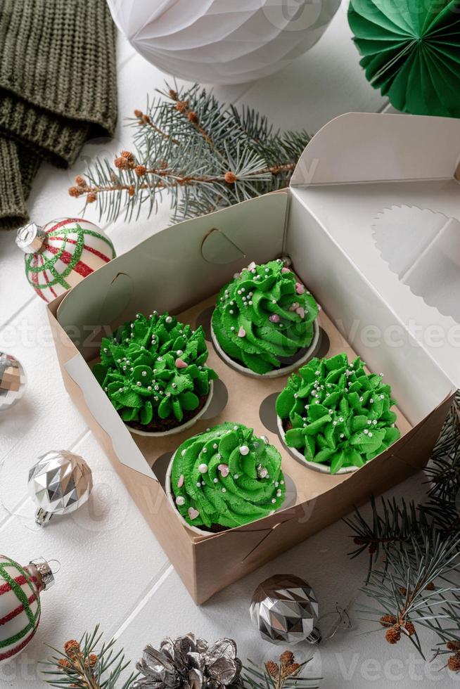 Cupcakes em forma de árvore de Natal em caixa ecológica artesanal, cercados de decorações festivas foto