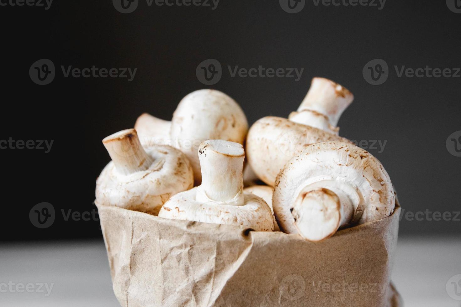 cogumelos champignon em saco de papel em uma mesa de madeira branca sobre um fundo escuro foto