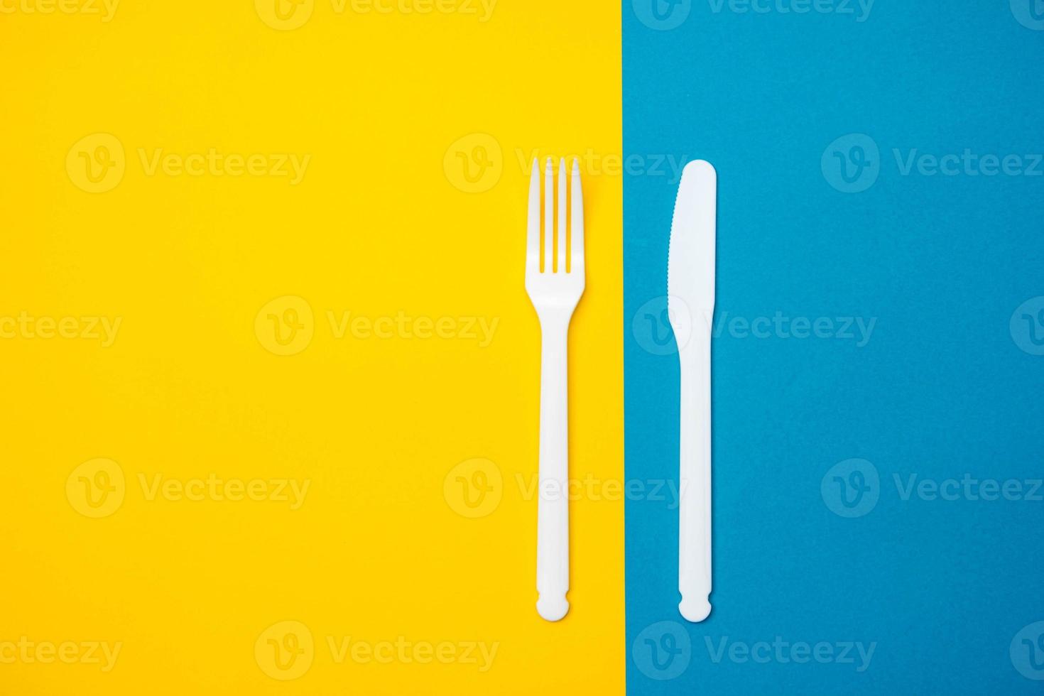 garfo e faca de plástico branco sobre fundo amarelo e azul. Utensílio de cozinha foto