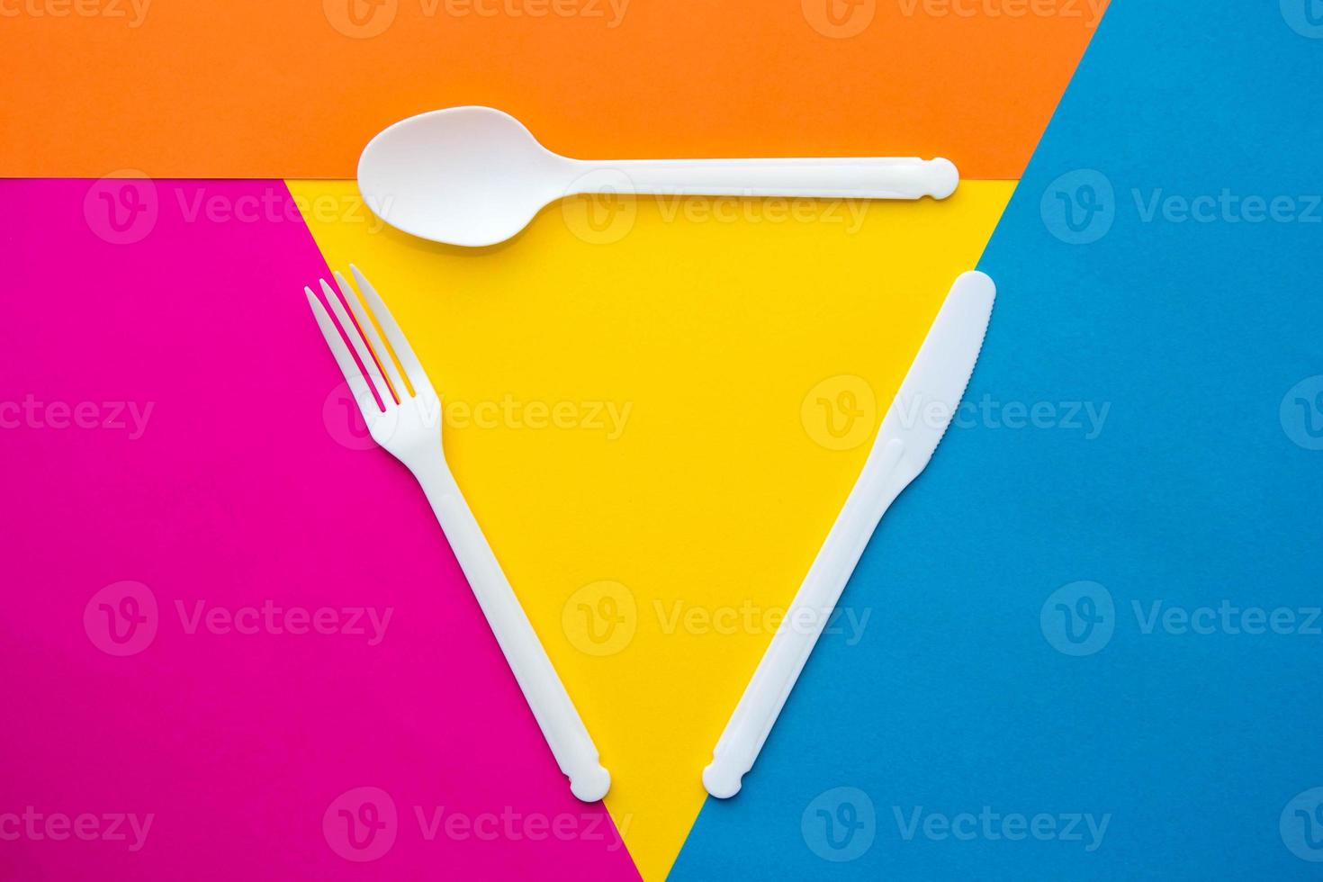 garfo, faca e colher de plástico branco em fundo multicolorido foto