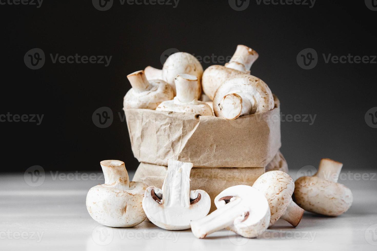 cogumelos champignon em saco de papel em uma mesa de madeira branca sobre um fundo escuro foto