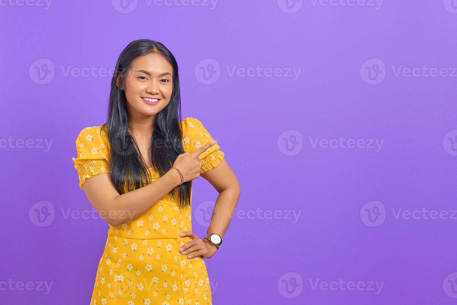 retrato de uma jovem asiática sorridente apontando o dedo para o espaço da cópia em fundo roxo foto