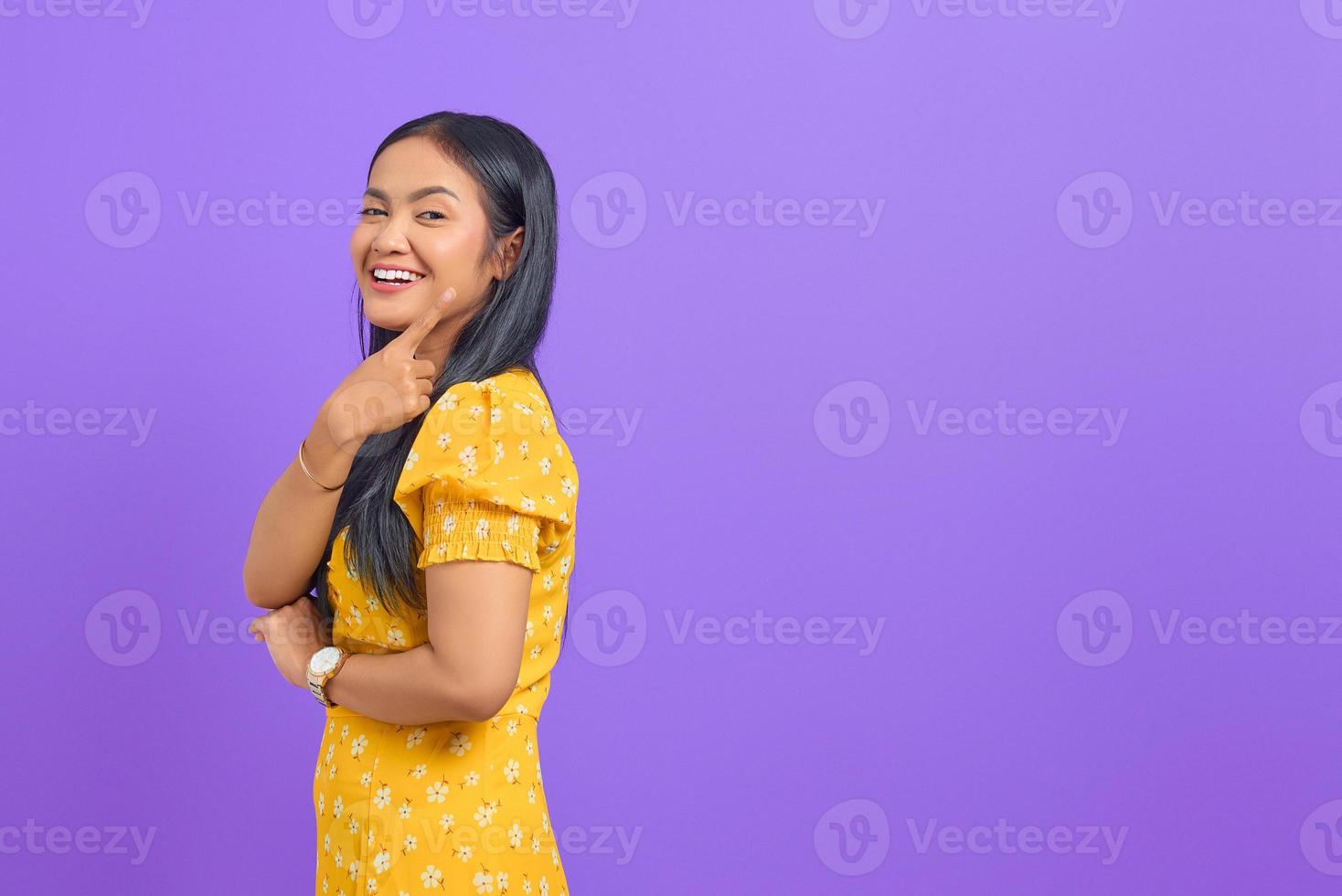 retrato de uma jovem asiática sorridente apontando o dedo para o espaço da cópia em fundo roxo foto