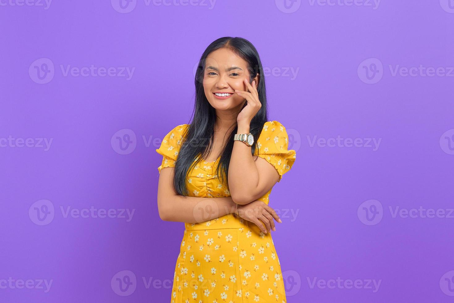 jovem asiática sorridente usando um vestido amarelo e parecendo confiante em um fundo roxo foto