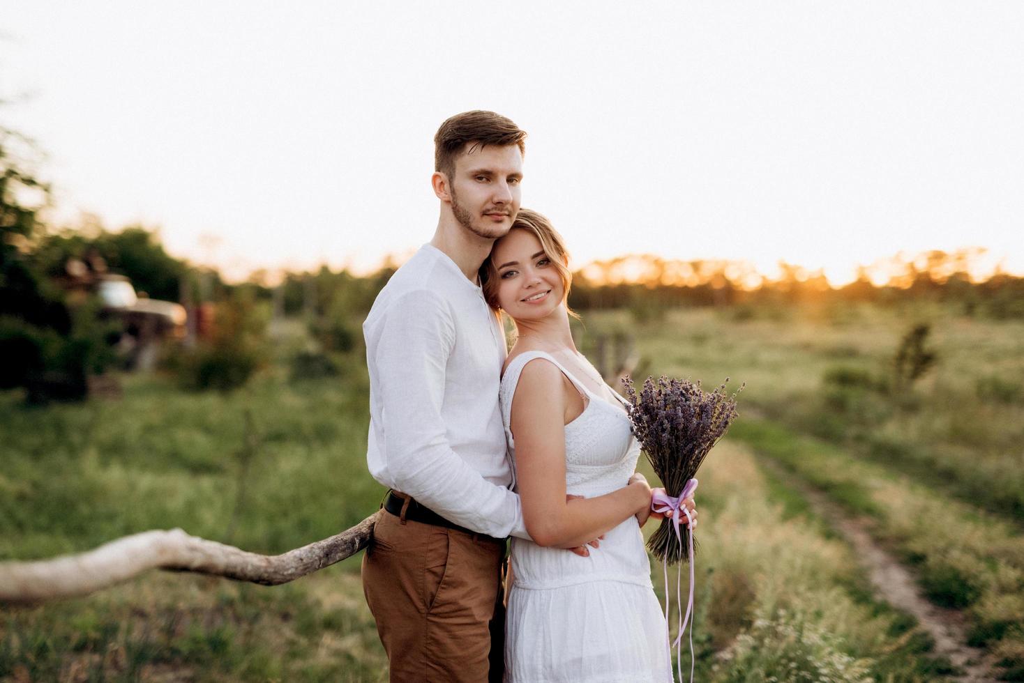 garota com um vestido de verão branco e um cara com uma camisa branca em uma caminhada ao pôr do sol com um buquê foto