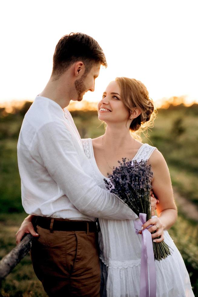 garota com um vestido de verão branco e um cara com uma camisa branca em uma caminhada ao pôr do sol com um buquê foto