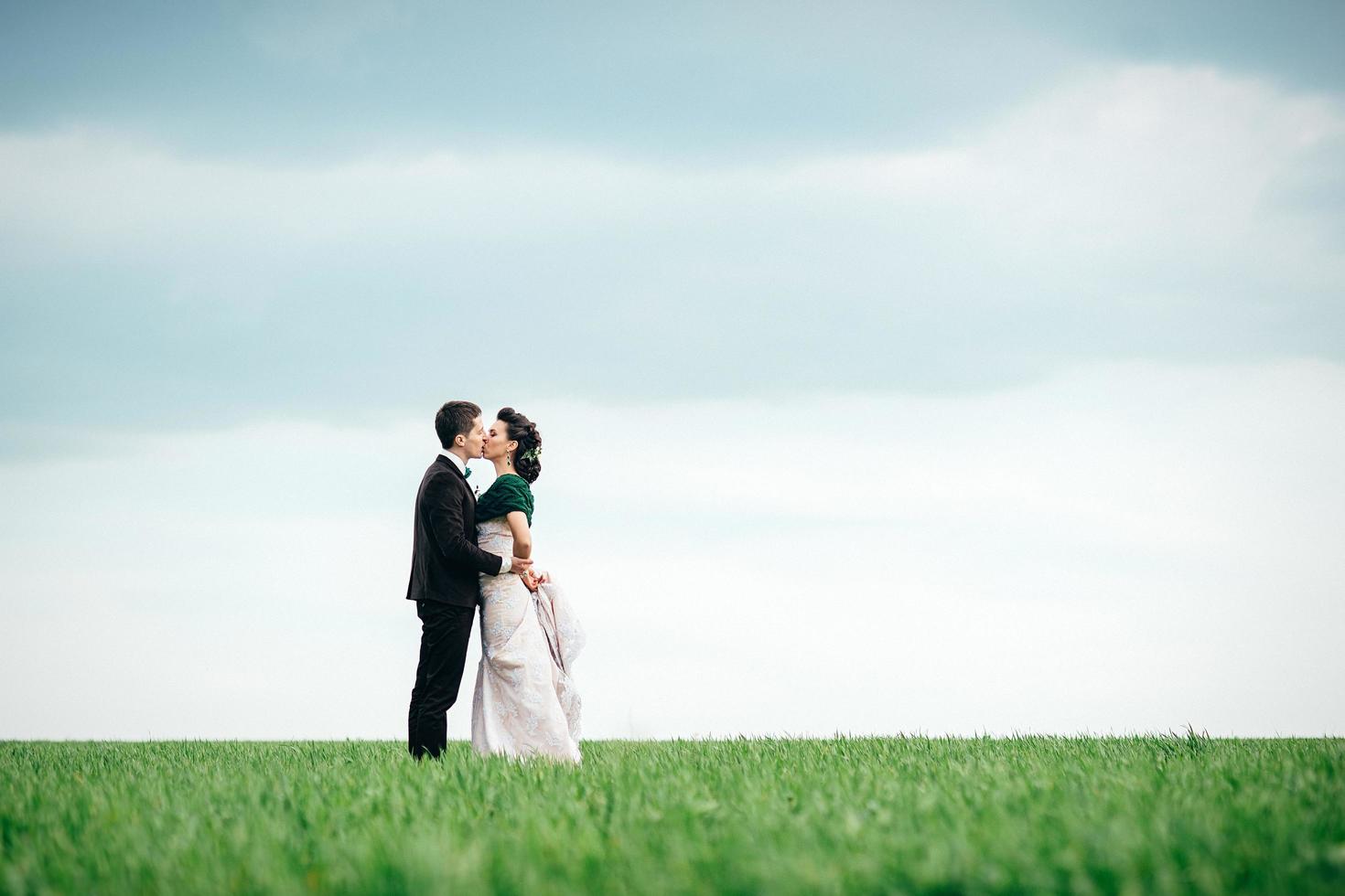 o noivo em um terno marrom e a noiva em um vestido cor de marfim em um campo verde foto