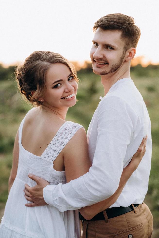 garota com um vestido de verão branco e um cara com uma camisa branca em uma caminhada ao pôr do sol com um buquê foto