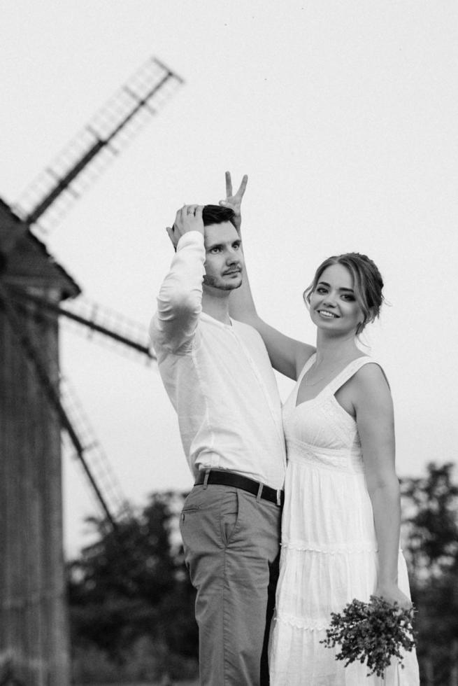 garota com um vestido de verão branco e um cara com uma camisa branca em uma caminhada ao pôr do sol com um buquê foto