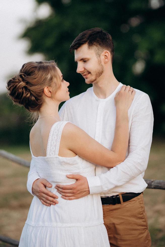 garota com um vestido de verão branco e um cara com uma camisa branca em uma caminhada ao pôr do sol com um buquê foto