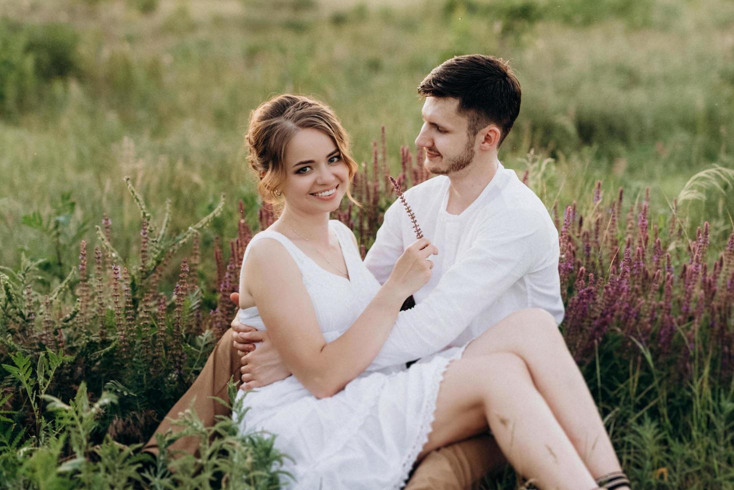 garota com um vestido de verão branco e um cara com uma camisa branca em uma caminhada ao pôr do sol com um buquê foto