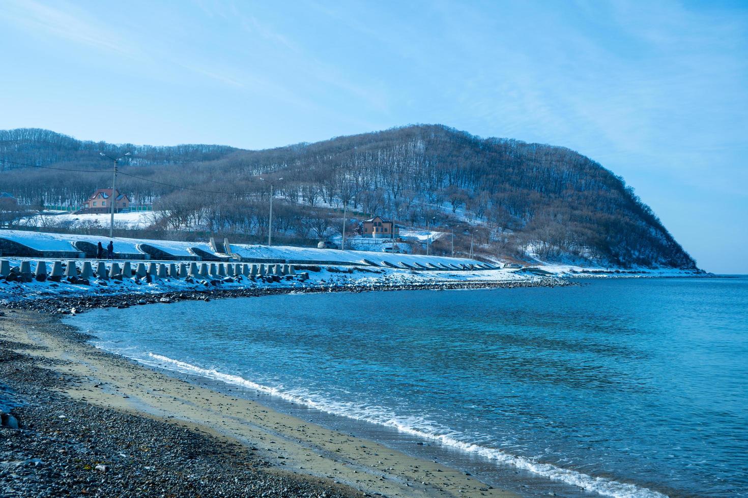 vista do mar com uma praia coberta de neve em um fundo de rocha. foto