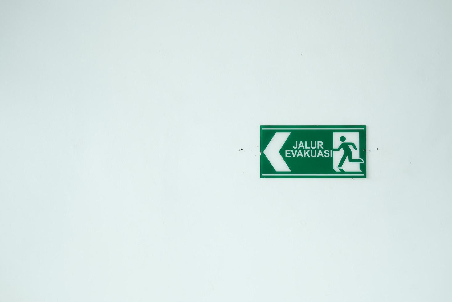 o sinal da rota de evacuação em cor verde está pendurado em uma parede branca. o signo essencial dos lugares públicos. foto