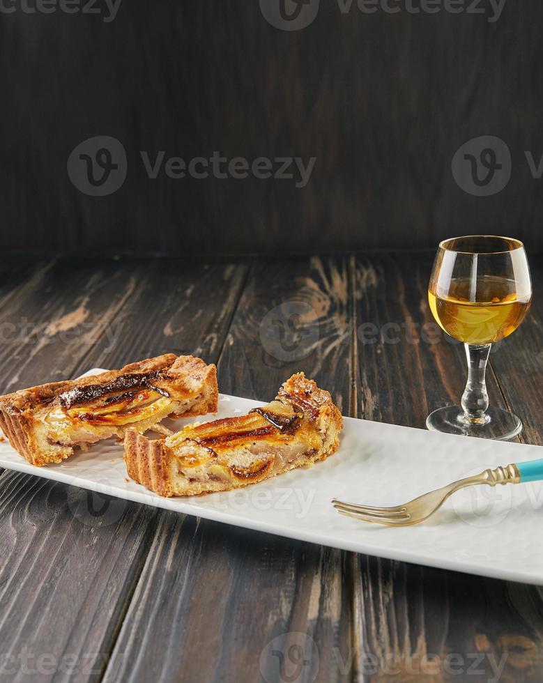 torta de maçã com fatias de baunilha em fatias com copo de licor, sobre fundo de madeira. comida gourmet francesa foto