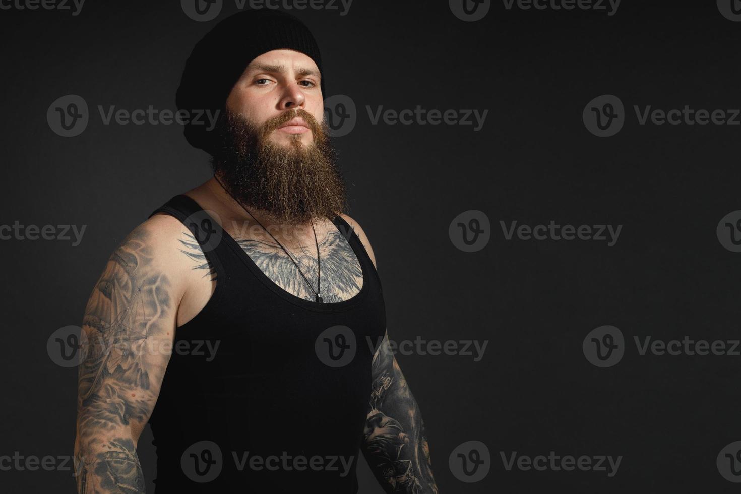 retrato de um homem barbudo bonito em uma camiseta preta e chapéu olhando para a câmera foto