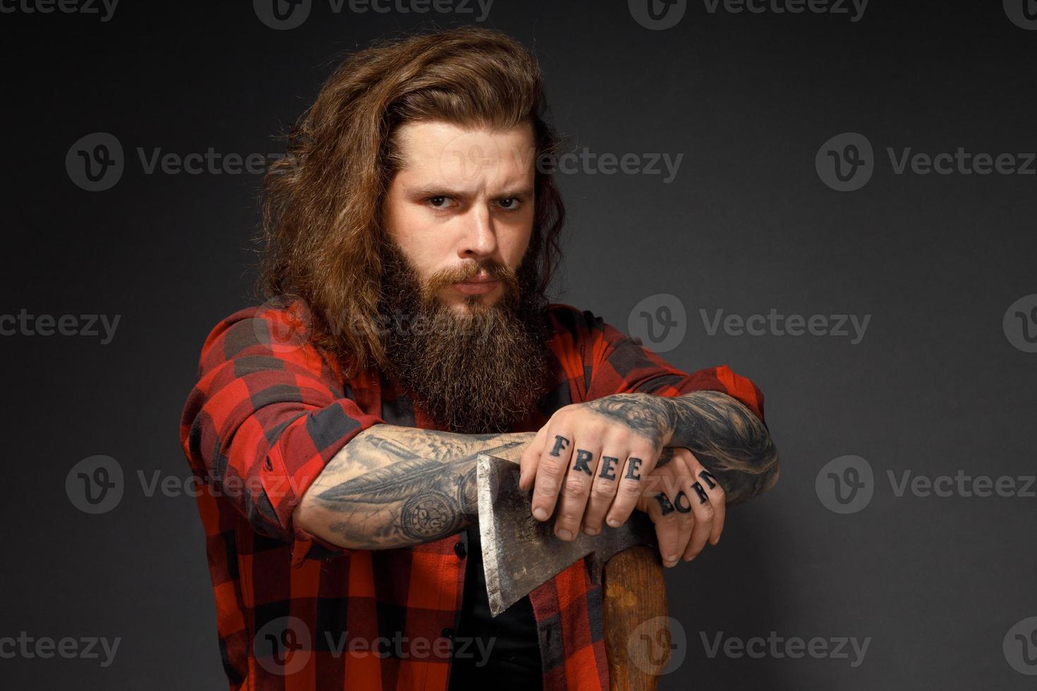 homem bonito com cabelo comprido com um machado nas mãos em um fundo escuro de estúdio foto