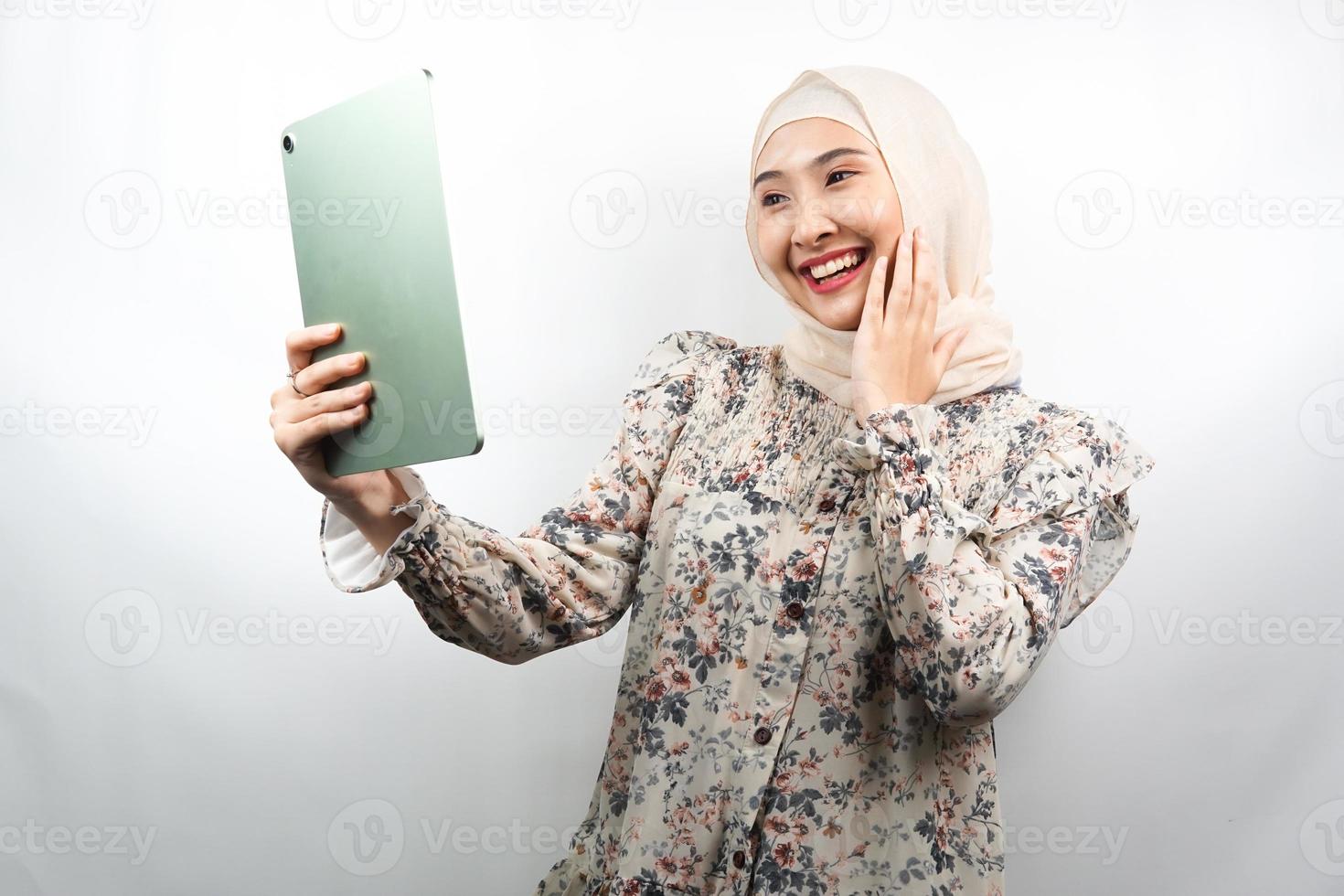 bela jovem asiática muçulmana sorrindo, animada e alegre segurando o tablet, isolado no fundo branco foto