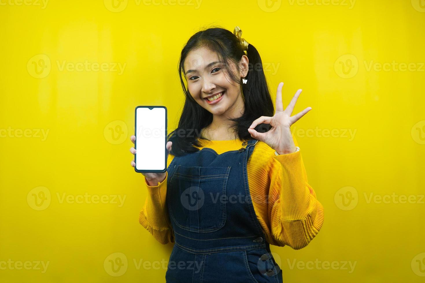 jovem bonita e fofa alegre, confiante, com as mãos segurando um smartphone, com smartphone com tela em branco ou branco, promovendo aplicativo, promovendo produto, propaganda, isolado foto