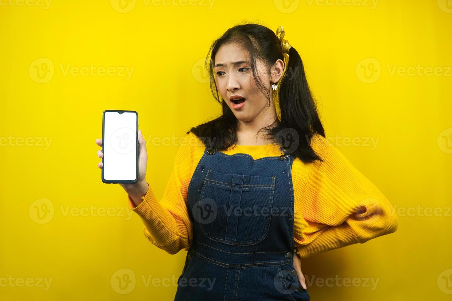 Mulher jovem bonita e fofa surpresa, chocada, expressão uau, mãos segurando um smartphone, com tela em branco ou branca do smartphone, promoção de aplicativo, promoção de produto, propaganda, isolado foto