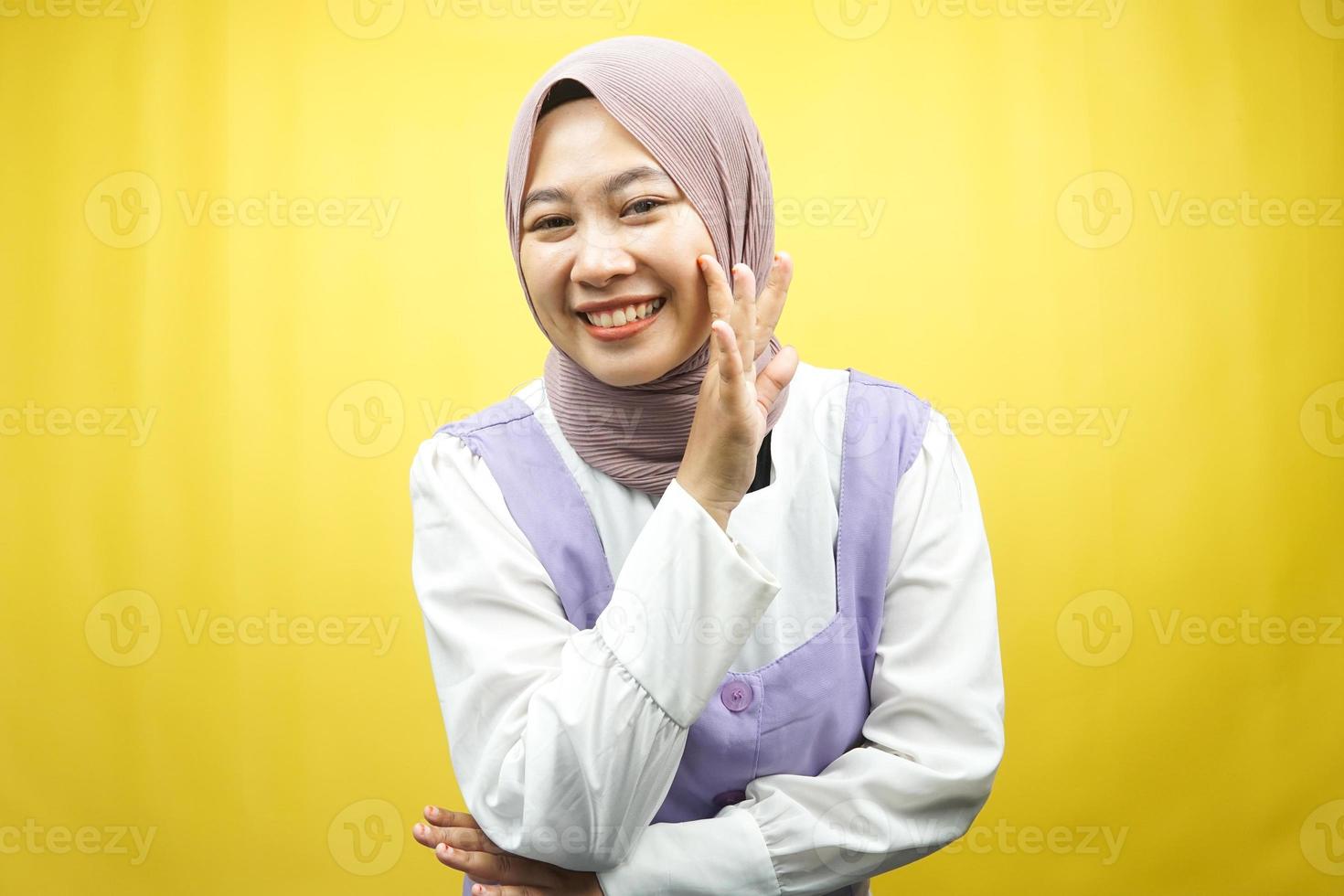 bela jovem asiática muçulmana sorrindo com confiança e entusiasmo perto da câmera, sussurrando, contando segredos, falando baixo, silencioso, isolado no fundo amarelo foto