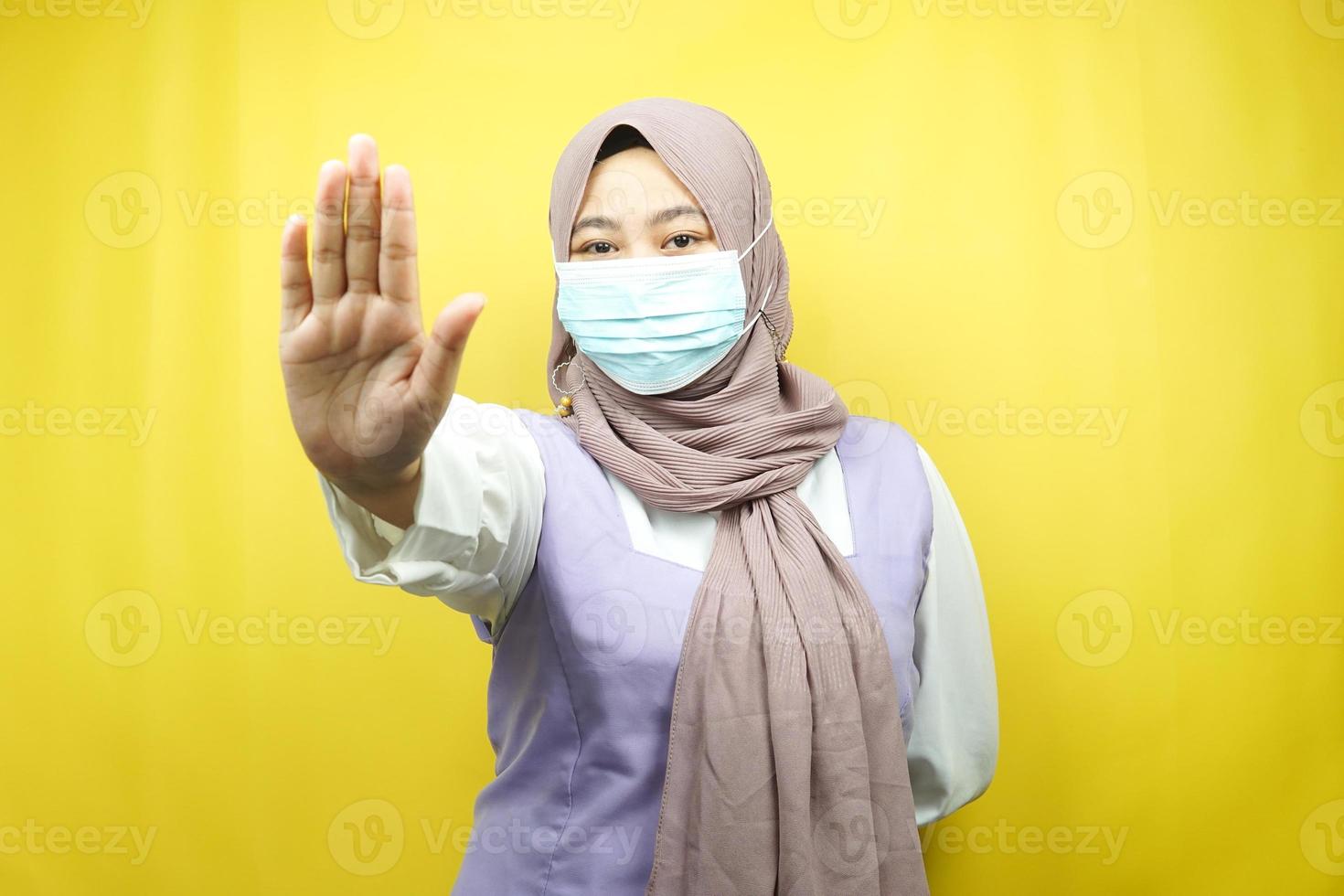 mulher muçulmana usando máscara médica, com sinal de parada, sinal de rejeição, não manter distância, sinal de não se aproximar, isolado em fundo amarelo foto