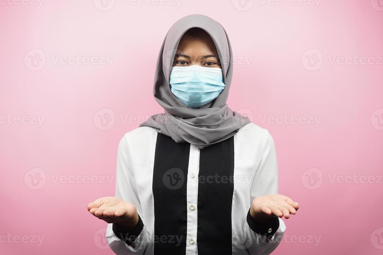 mulher muçulmana usando máscara médica, apresentando algo com as mãos, isolado em um fundo rosa foto