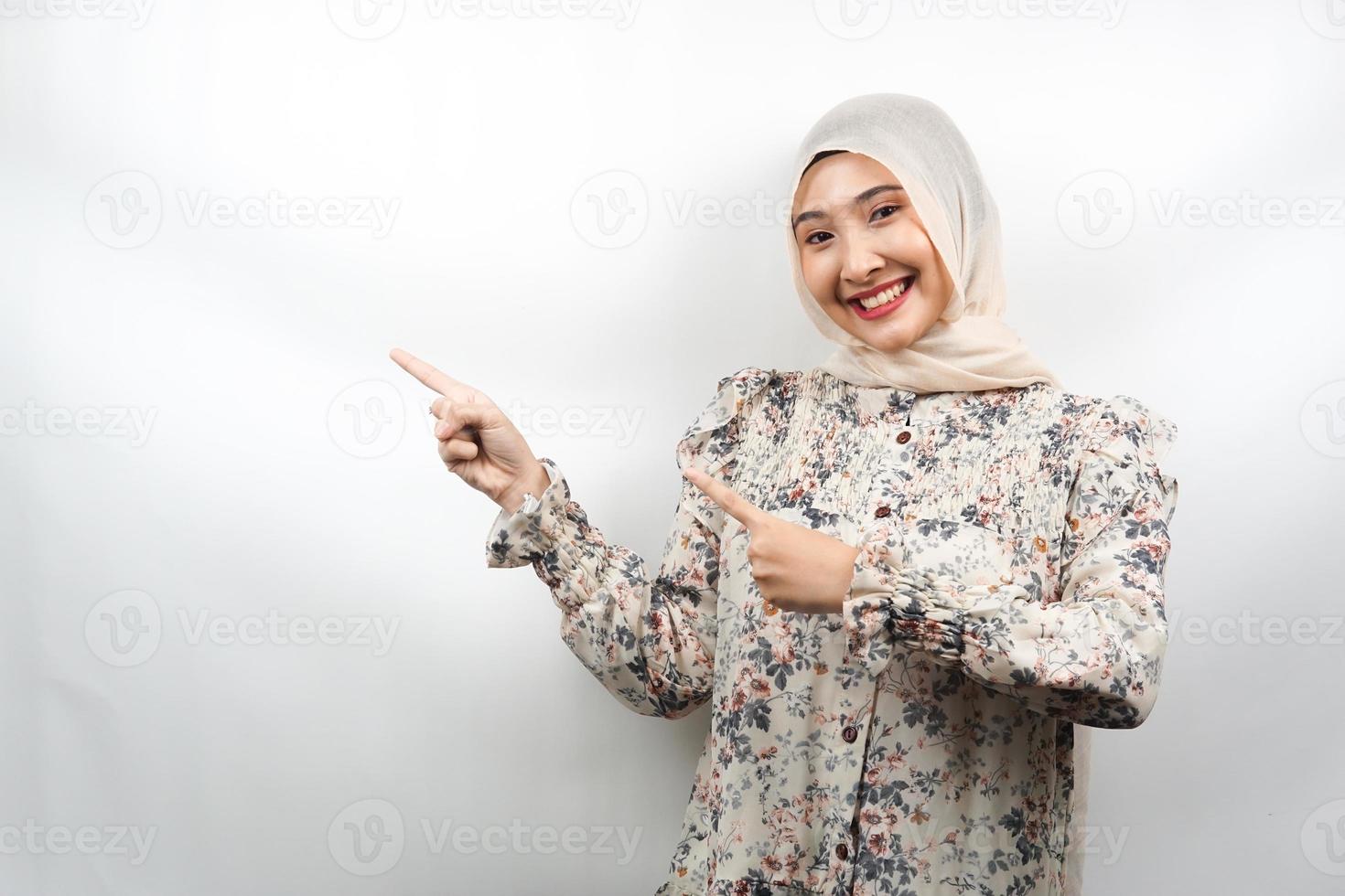 bela jovem asiática muçulmana sorrindo confiante, entusiasmada e alegre com as mãos apontando o espaço vazio, apresentando algo voltado para a câmera, isolada no fundo branco, conceito de publicidade foto