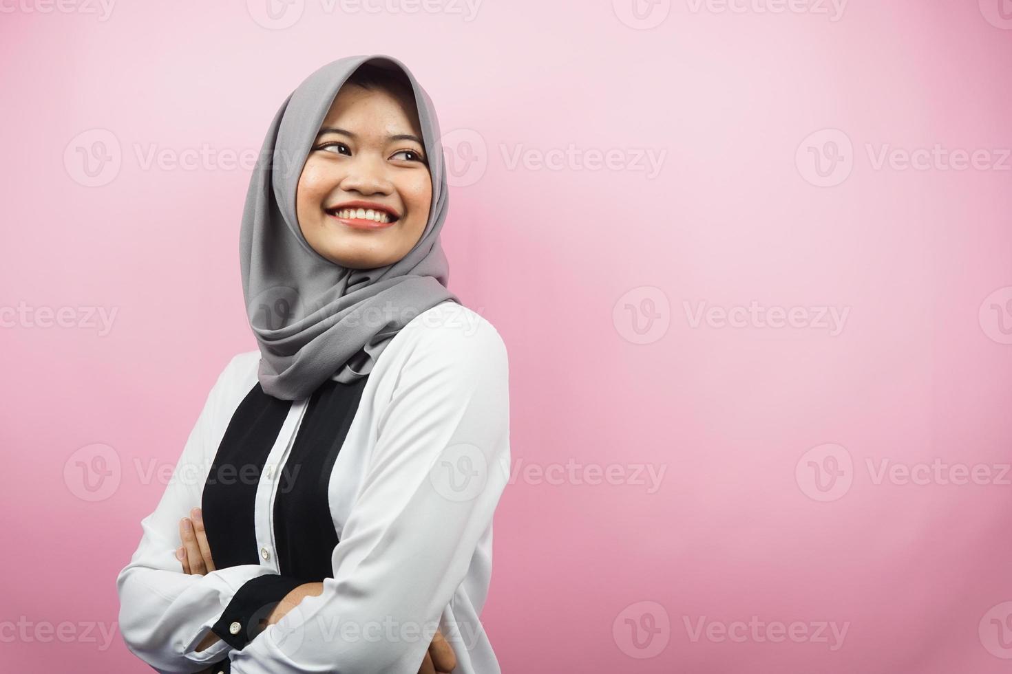 linda jovem asiática muçulmana confiante e alegre, olhando o espaço vazio, apresentando algo, isolado no fundo rosa foto