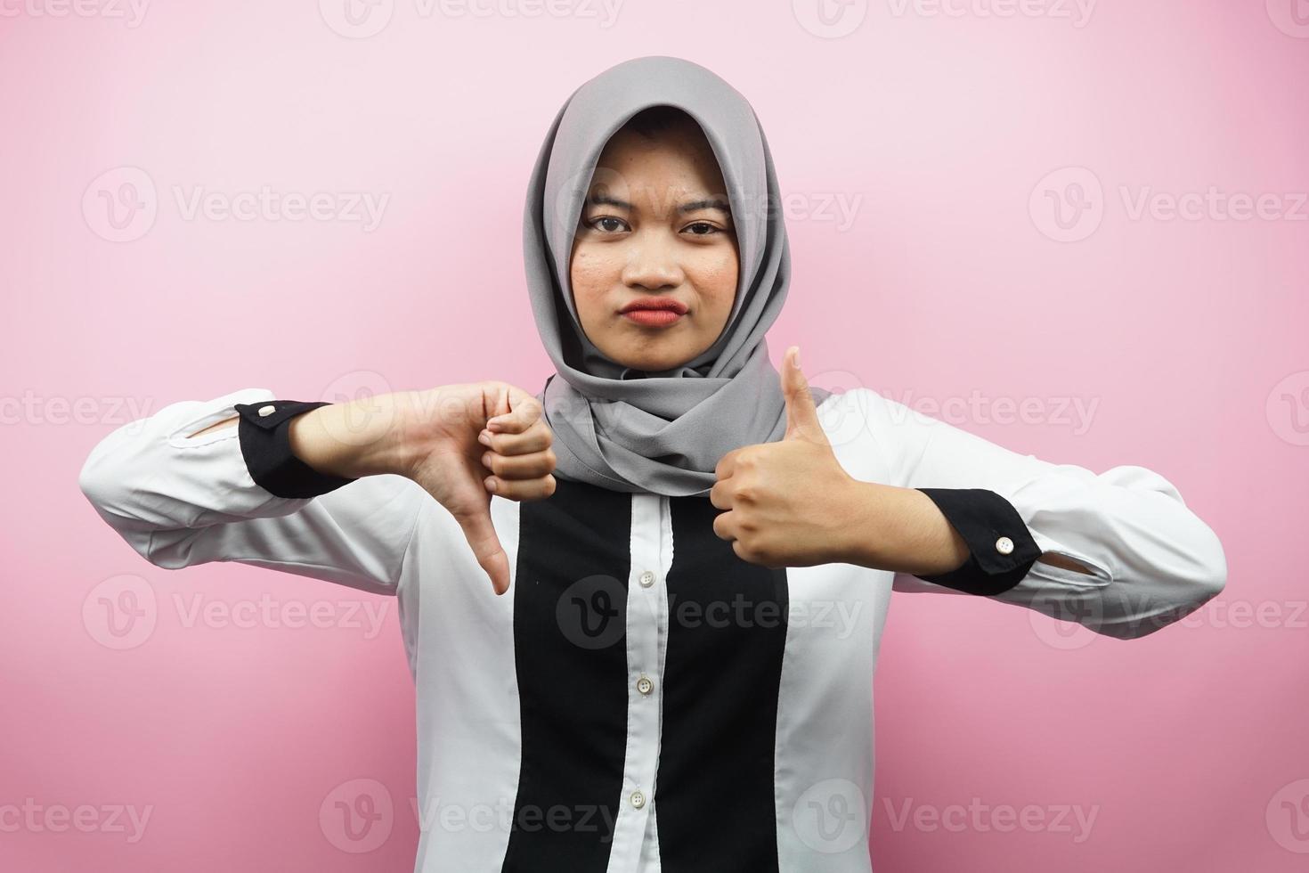 linda jovem muçulmana asiática com sinal de mão de gosta ou não gosta, sim ou não, feliz ou triste, comparando duas coisas, isolado no fundo rosa foto