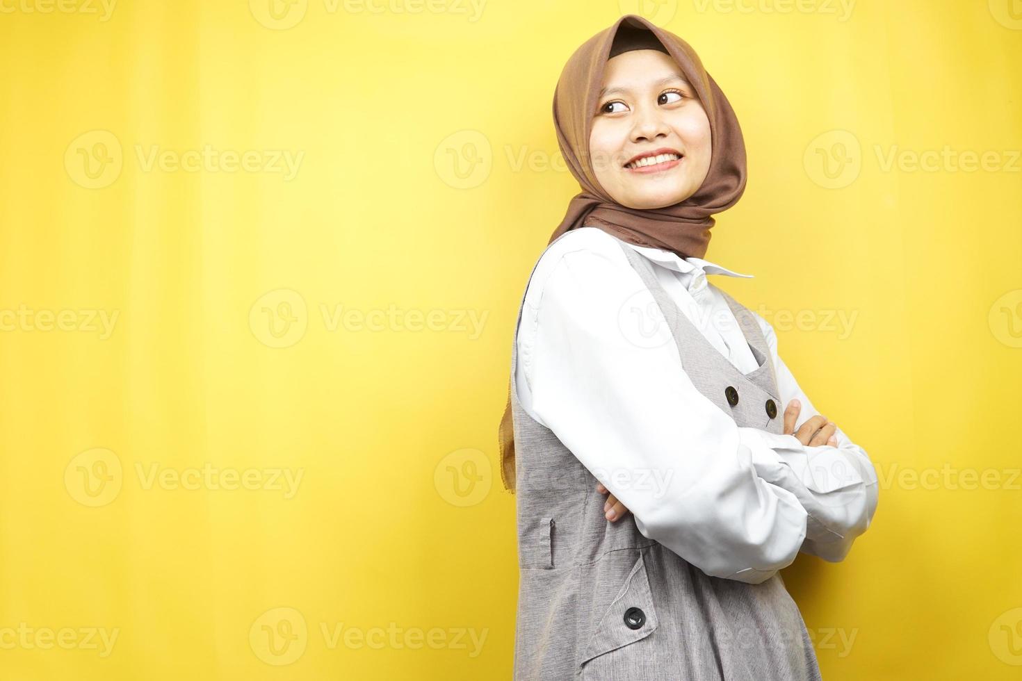 linda jovem asiática muçulmana confiante e alegre, procurando o espaço vazio, apresentando algo, isolado em um fundo amarelo foto