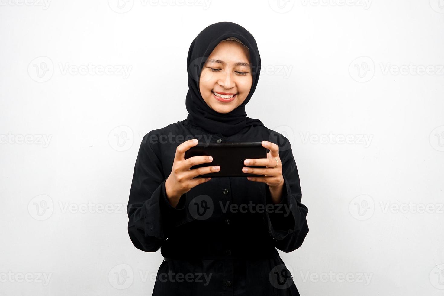 linda jovem muçulmana asiática com as mãos segurando um smartphone, jogando, sorrindo feliz, vitória, sucesso, isolado no fundo branco, conceito de publicidade foto