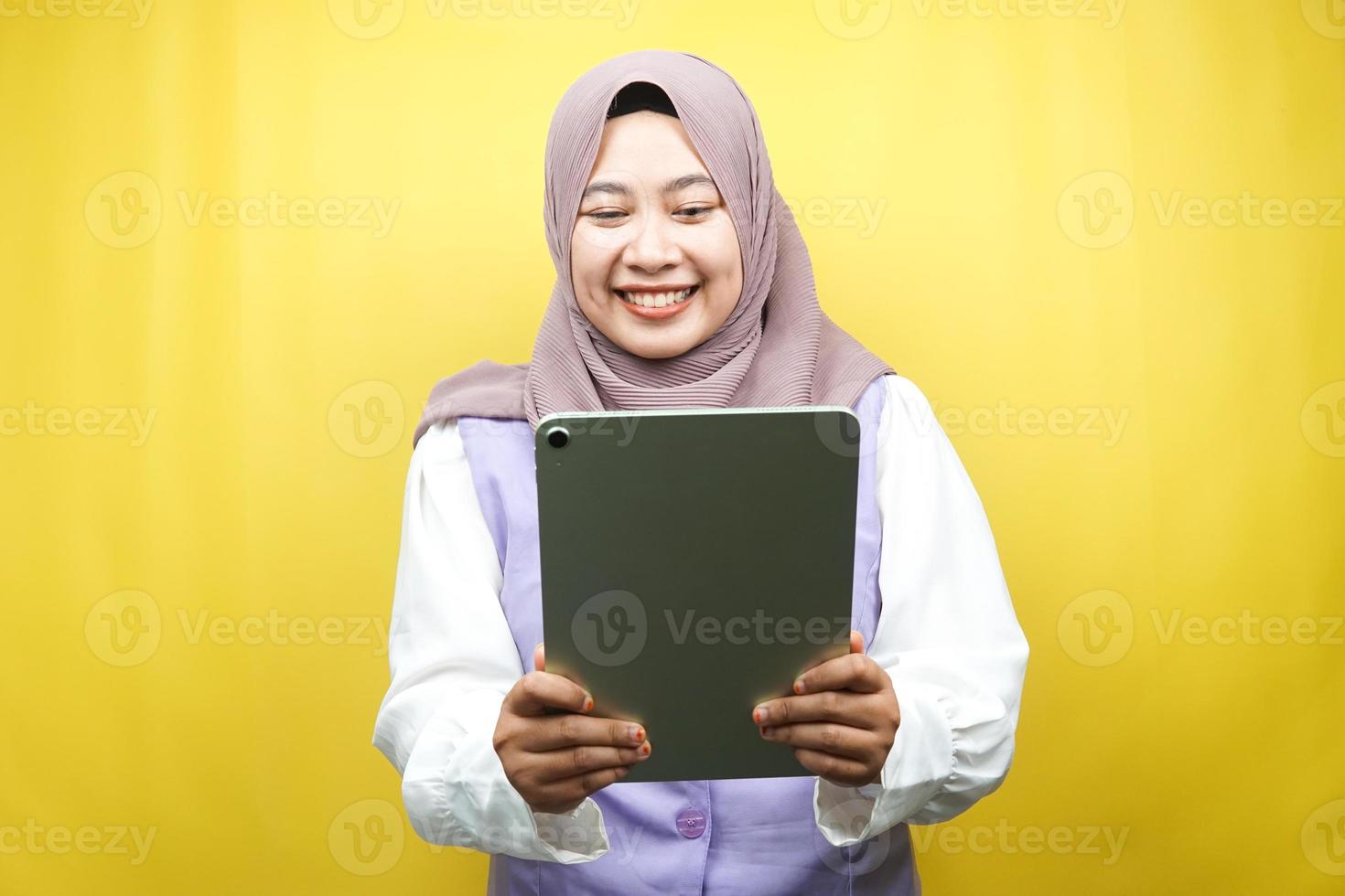 bela jovem asiática muçulmana sorrindo, animada e alegre segurando o tablet, isolado em um fundo amarelo foto