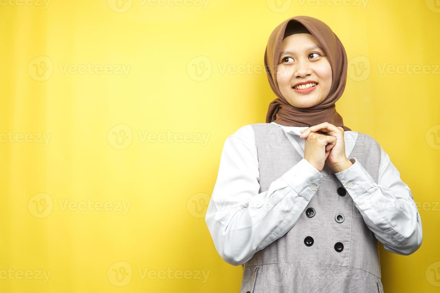 linda jovem asiática muçulmana confiante e alegre, procurando o espaço vazio, apresentando algo, isolado em um fundo amarelo foto